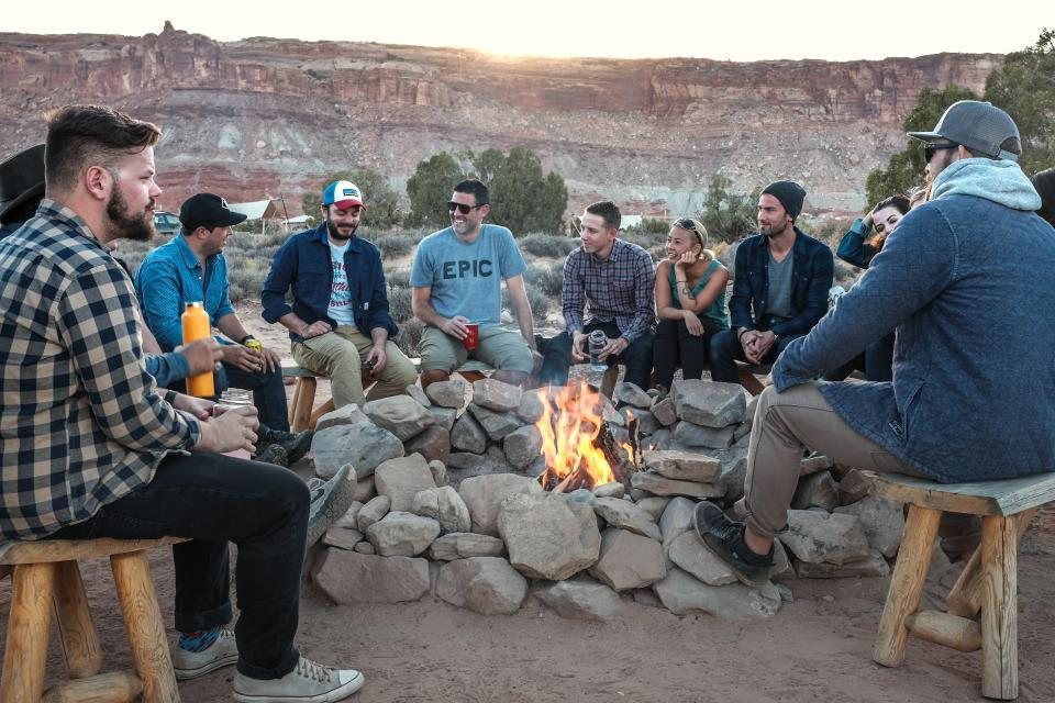 Illustrative image: a group of friends talking around a campfire in a desert canyon at sunset